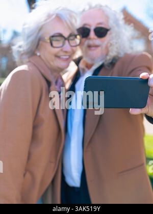 Senior couple taking selfie outdoors with smartphone, smiling and wearing sunglasses Stock Photo