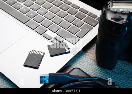 USB cable, SD memory cards, camera and laptop on wooden table, closeup Stock Photo