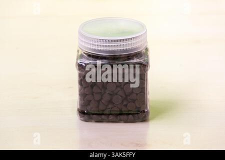 Chocolates in a transparent plastic jar sit on a light wooden surface, forming a triangular shape. They look very delicious and can also be used to de Stock Photo