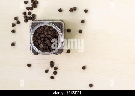 Top view of chocolates in a plastic jar on a wooden background. Round and triangular dark chocolate pieces, very tasty. Can be used to decorate birthd Stock Photo
