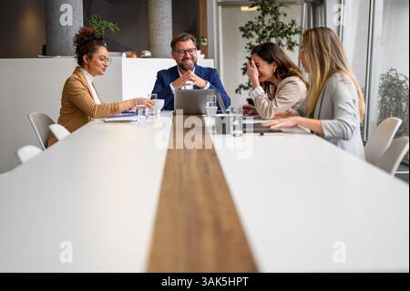 Professional team members smiling and discussing around conference table during collaborative meeting Stock Photo