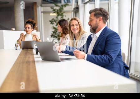 Businessman working on laptop and discussing ideas with female colleague during meeting in office Stock Photo