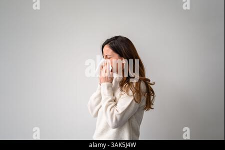 Side view of young woman feeling unwell and blowing her nose into a handkerchief on isolated white background Stock Photo