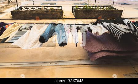 Clothes hang on a laundry line outside a residential building in Lisbon, Portugal, with stone planters and balconies, capturing the everyday life and Stock Photo