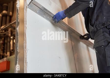 A view from below of a man holding a metal rule in his hands and leveling a newly plastered wall. With space to copy. High quality photo Stock Photo
