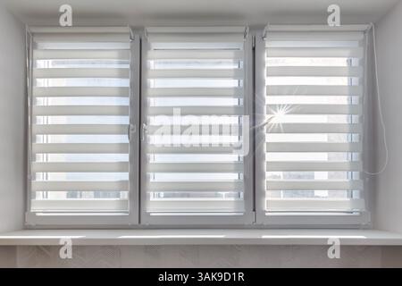 Modern double roller zebra blinds on large windows in bright minimalist interior with sunlight streaming through on balcony Stock Photo
