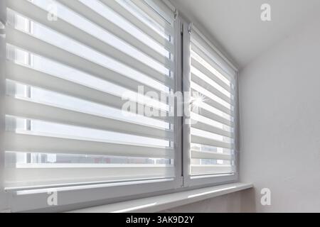 Modern double roller zebra blinds on large windows in bright minimalist interior with sunlight streaming through on balcony Stock Photo