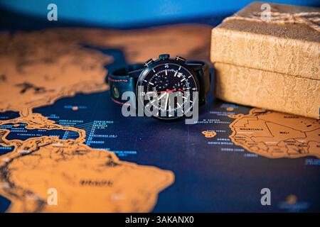 A black wristwatch placed on a travel map next to a piece of sandstone, symbolizing time and exploration Stock Photo