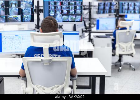 Security officer monitoring multiple surveillance screens in a high-tech control room for safety and surveillance Stock Photo