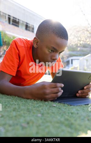 Lying on grass, boy using tablet for studying outside school building Stock Photo
