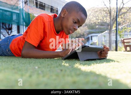 Using tablet, boy lying on grass in school, focusing on screen Stock Photo
