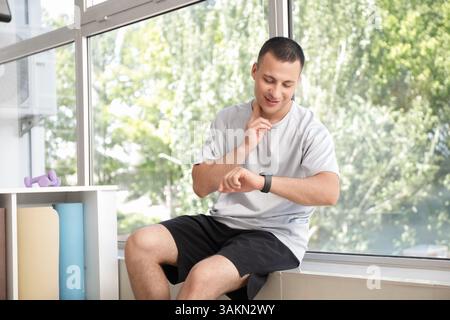 Sporty young man checking pulse near window in gym Stock Photo