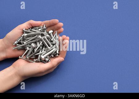 Female hands holding pile of different tap bolts and screws on blue background Stock Photo
