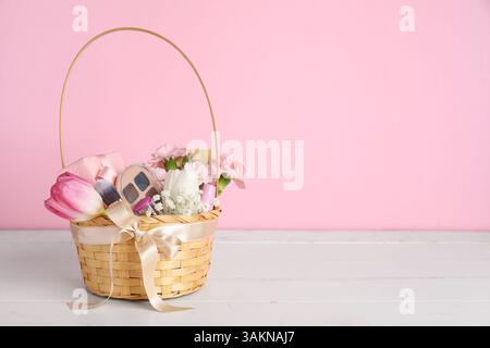 Wicker basket with beautiful flowers, gift boxes and decorative cosmetics on light wooden table Stock Photo