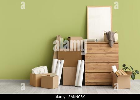 Chest of drawers with blank frame and cardboard boxes near green wall in room on moving day Stock Photo