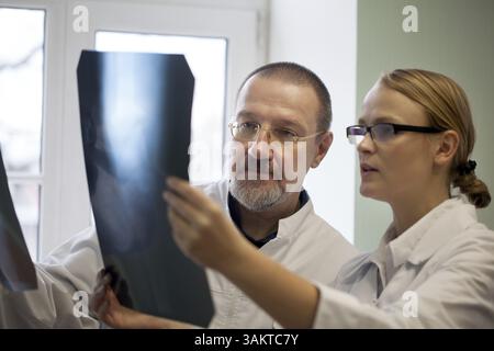 Young and experienced doctors looking at two x-ray images and trying to make a right diagnosis Stock Photo