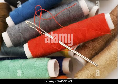 Many bobbins with different colored threads and needle Stock Photo