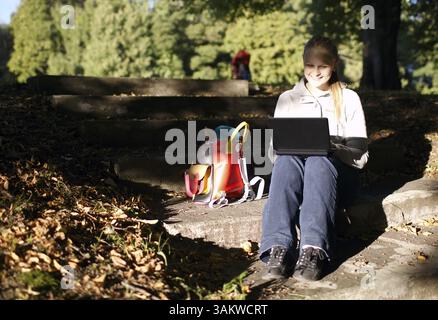 Young woman working outdoors on a laptop computer sitting on steps in the garden in late evening sunlight, enjoying the peace of nature Stock Photo