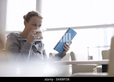 Young woman using her touchpad while drinking coffee in cafe Stock Photo