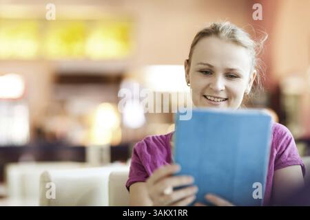 Young smiling woman in cafeteria using tablet computer Stock Photo