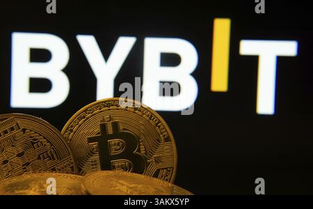 Dhaka, Bangladesh- 11 April 2025: Close-up of Bitcoin coins with the Bybit logo visible on a screen in the background Stock Photo