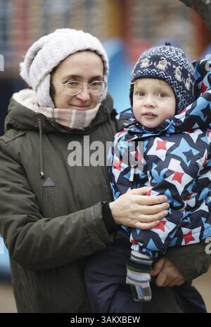 Middle-aged woman holding her cute young son in her arms on a cold winter day both dressed in thick warm winter clothes as they smile at the camera Stock Photo