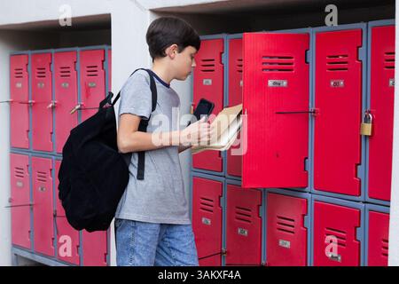 Opening locker, boy with backpack holding books and smartphone at school, copy space Stock Photo