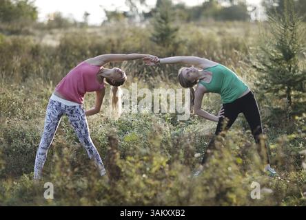 Two supple athletic young women working out together in the countryside doing bending and stretching exercises Stock Photo