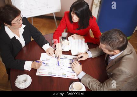 High angle view of a dedicated business team of two women and a man seated at a table having a meeting brainstorming a new project and analysing a doc Stock Photo