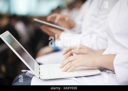 Woman and man doctors or medical students on the lecture or symposium. They using laptop and digital tablet. Focus on female hands typing on portable Stock Photo