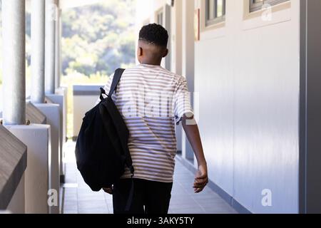 Walking in school hallway, boy carrying backpack and wearing striped shirt Stock Photo