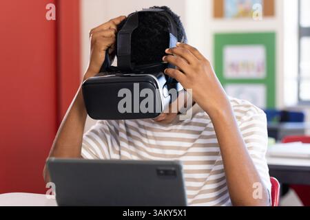 Using VR headset, student exploring virtual reality with tablet in school classroom Stock Photo