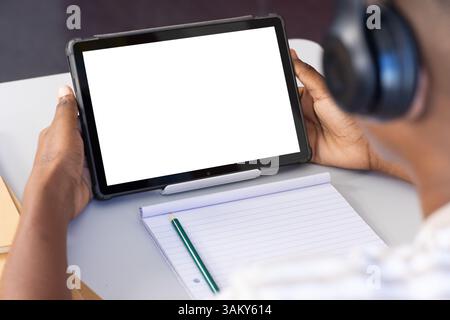 Using tablet with headphones, student taking notes in school classroom, copy space Stock Photo