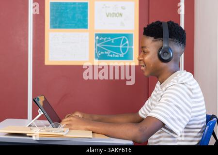 Using tablet and wearing headphones, boy studying in school classroom Stock Photo