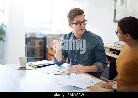People, desk and documents with talking for startup or business, creative or editor for magazine. Team, entrepreneurs and working at table with paper Stock Photo