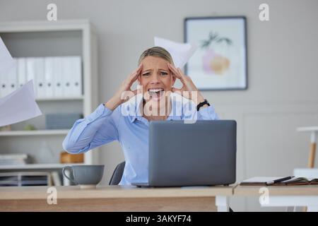 Stressed, frustrated and screaming businesswoman working on a laptop in her corporate office. Professional, worried and overworked female in a crisis Stock Photo