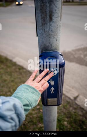 Human hand pressing crosswalk button on traffic light pole in urban area. pedestrian safety concept Stock Photo