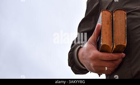A person holds two worn, aged books in their hand against a blurred, light background. Stock Photo
