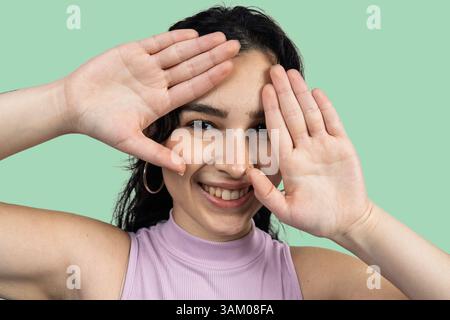 Cheerful young woman framing her face with hands and smiling on a green background Stock Photo