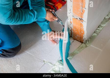 Construction worker is cutting edge insulation panel using utility knife during floor installation Stock Photo