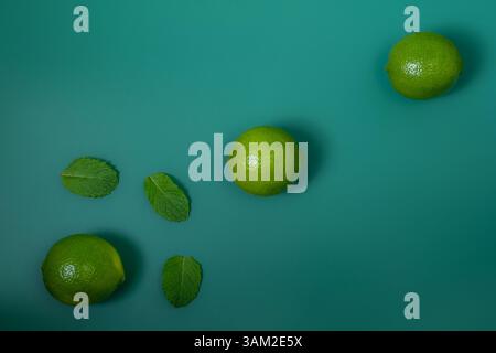 Three Limes Diagonally Aligned with Mint Leaves on Green Background – Top View Stock Photo