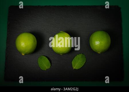 Three Limes on Black Slate with Mint Leaves – Top View Stock Photo