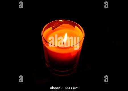 A bright orange candle in a glass candlestick, burning in the dark Stock Photo