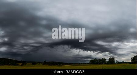 A surreal formation of storm clouds spreads across the sky above Lithuanian meadows. The low, dark cloud base and shifting patterns in the sky give th Stock Photo