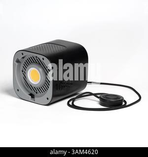 Black modern LED spotlight with heatsink fins and a remote control on a white surface, studio shot. Stock Photo