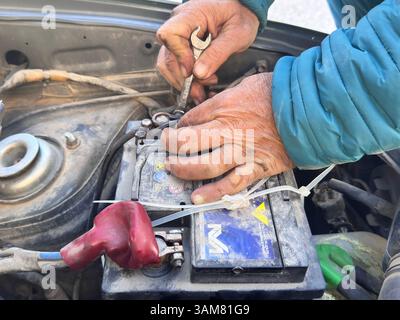 Man's hands trying to remove a damaged car battery using tools, such as wrenches Stock Photo