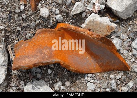 A discarded machine part lies in the gravel, rusty and marked by time - a symbol of transience, technology and industrial decay. Stock Photo