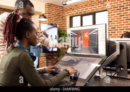 African american coworkers discussing innovative ideas at office desk, using graphic software for website development. Black male manager points to screen, explaining digital tools to female employee. Stock Photo