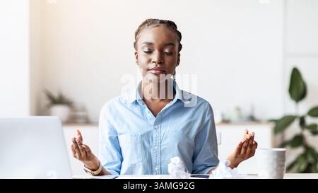 Coping With Stress At Work. Young African Businesswoman Meditating In Office Stock Photo