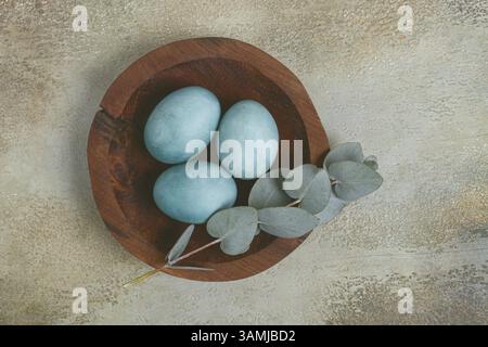 Easter colored eggs, in turquoise tones, on a wooden platter, with a branch of eucalyptus, Easter card, top view, without people Stock Photo